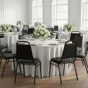 Dining room with round tables, black chairs, and white tablecloths.